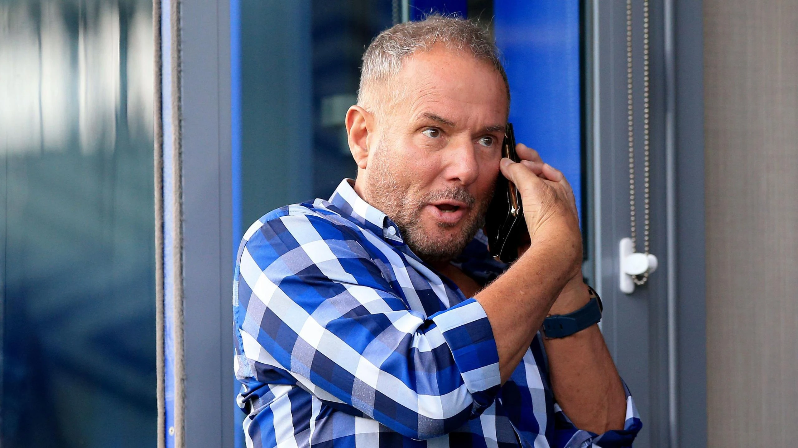 Derek Hatton with a checked blue shirt is on a mobile phone