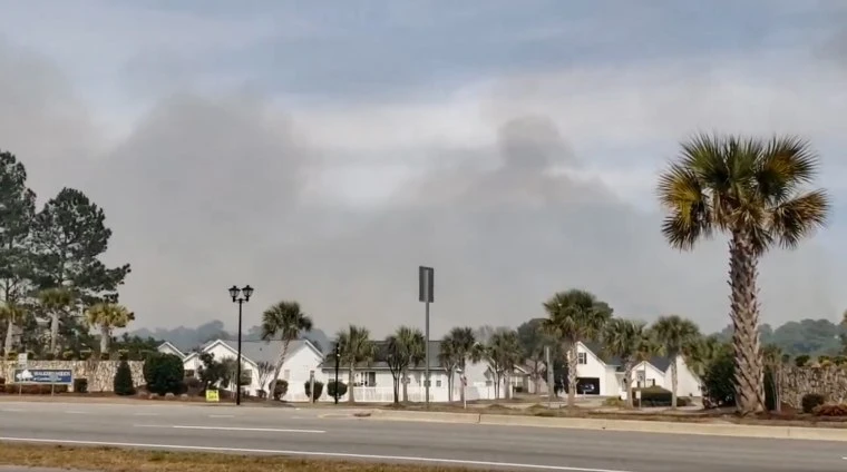 smoke plumes in the sky in the distance over houses seen from the street