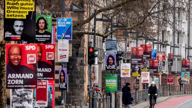 A sidewalk on a thoroughfare is shown with dozens of election campaign signs.