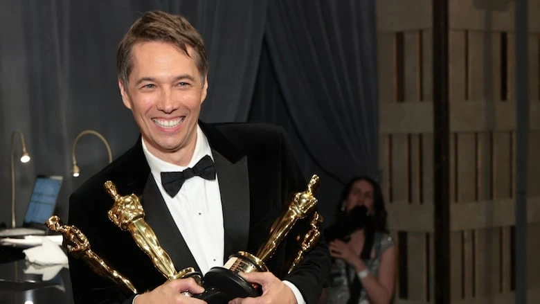 A man poses with four trophies.