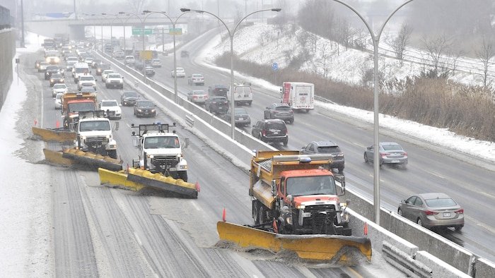 Photo de trois déneigeuses qui roulent sur l'autoroute DVP suivies d'une file de véhicules.