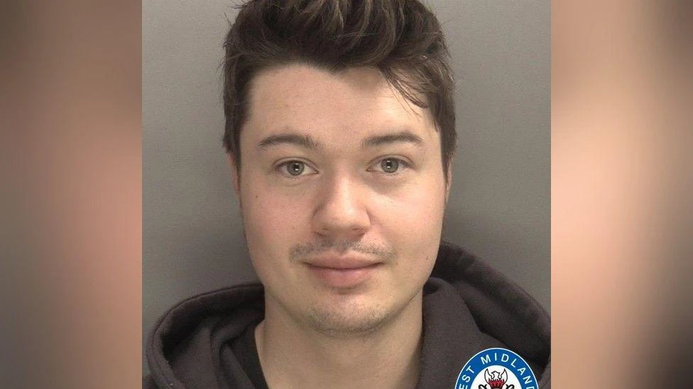 A mugshot of a man with short brown hair, wearing a black hoody