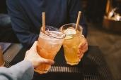 Friends clink cocktail glasses sporting paper straws.