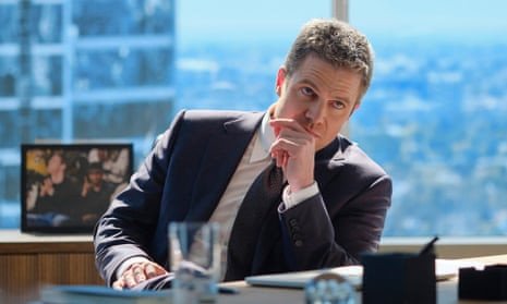 A man sitting at an office desk and wearing a suit looks up while resting his chin on his hand