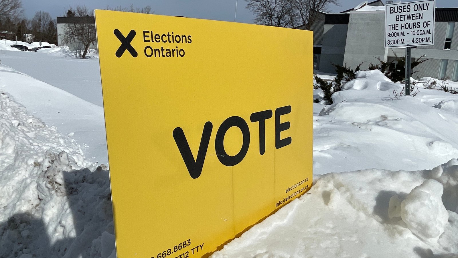 A yellow Elections Ontario sign that says "vote" is placed in a snowbank.