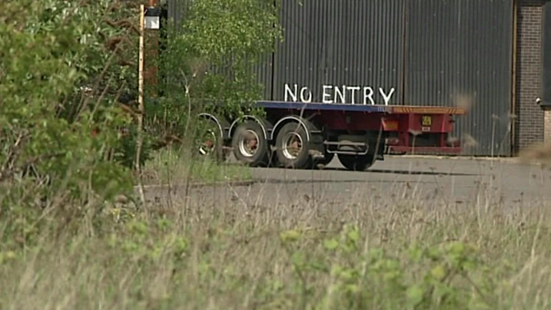 A truck trailers in a disused steelworks. Above the trailer is "NO ENTRY" written in white paint on a corrugated iron wall.