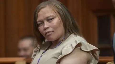 Getty Images Kelly Smith, dressed in a beige dress and wearing a purple necklace, looks on during court proceedings in her human trafficking case