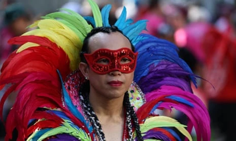 A young person wears a colourful headdress and a red mask before the start of the Sydney Gay and Lesbian Mardi Gras