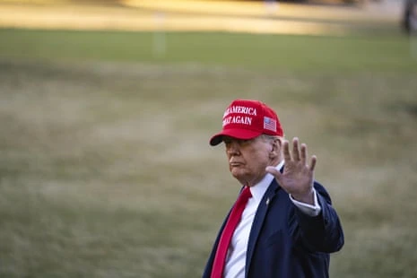 A man in a suit with a Maga hat on waves.