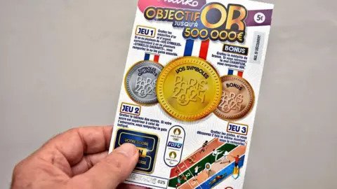 Getty Images A man's hand holding a French scratch card which is Paris Olympics themed.