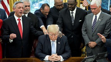 President Trump bowing his head in prayer with faith leaders and Vice President Pence in the Oval Office.