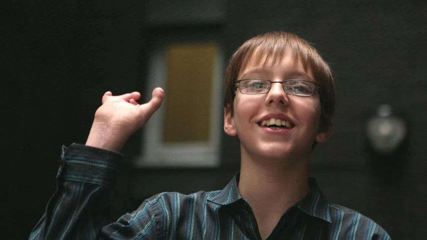 A young boy with a limb difference holds his hand in the air as he smiles