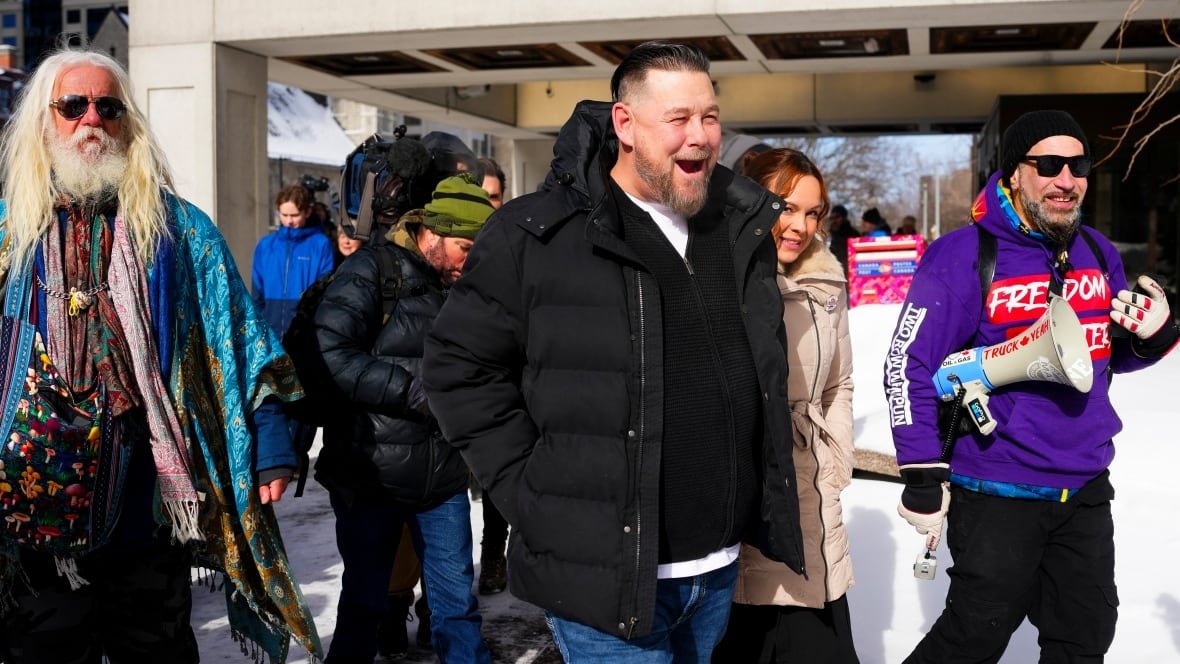 A bearded man smiles outside a courthouse in winter with a crowd around him.