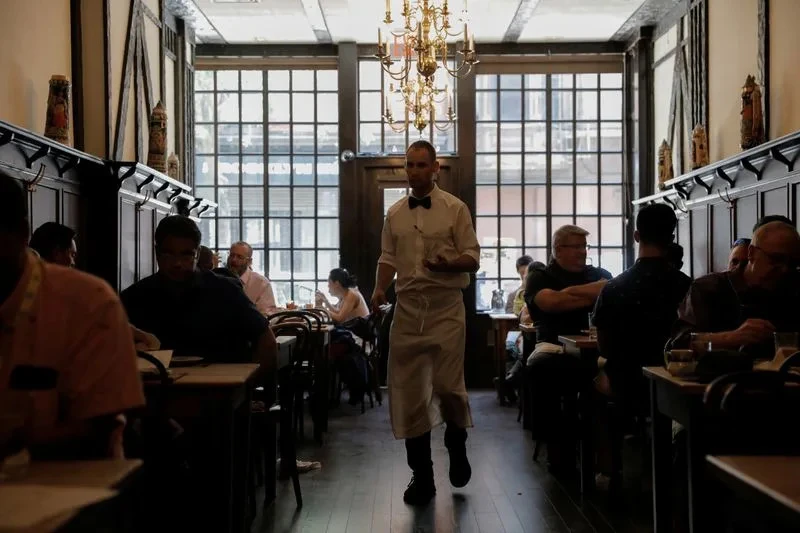 FILE PHOTO: A waiter walks among diners at Peter Luger Steak House in Brooklyn, New York City, as the US service sector expands, with Reuters capturing the scene.