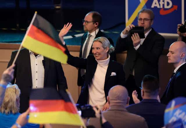 Alice Weidel waves at an AfD event, there are guests waving miniature German flags in the foreground