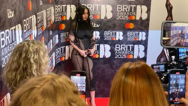 Charlie XCX poses with her Brits awards inside the Winners Room. She's wearing a see-through black dress with matching veil