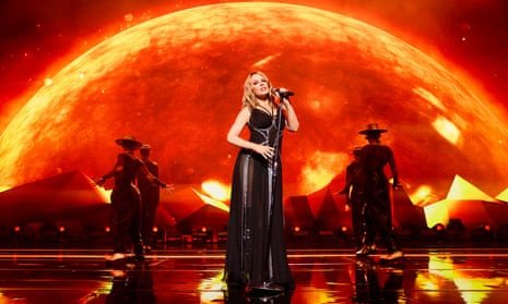 Kylie Minogue on stage against the backdrop of a burning sphere