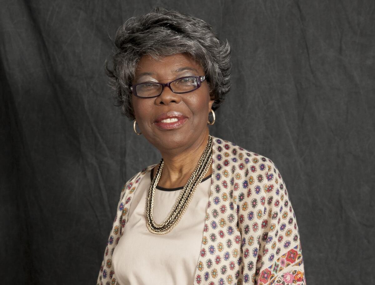 Voletta Wallace wearing glasses, hoop earrings and a smile